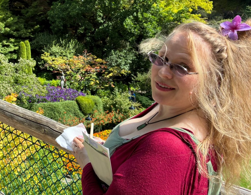 Charlie Wilson peeks over her sunglasses from on top of a bridge over a verdant garden.